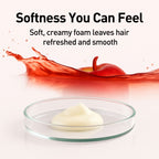 Creamy white substance in a glass dish with red liquid and apple in the background, labeled 'Softness You Can Feel'.