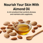 Almond oil in a glass bowl with almonds and a wooden spoon on a beige background.